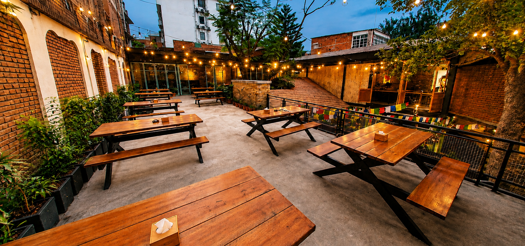 Garden courtyard with prayer flags, trees and warm string lights